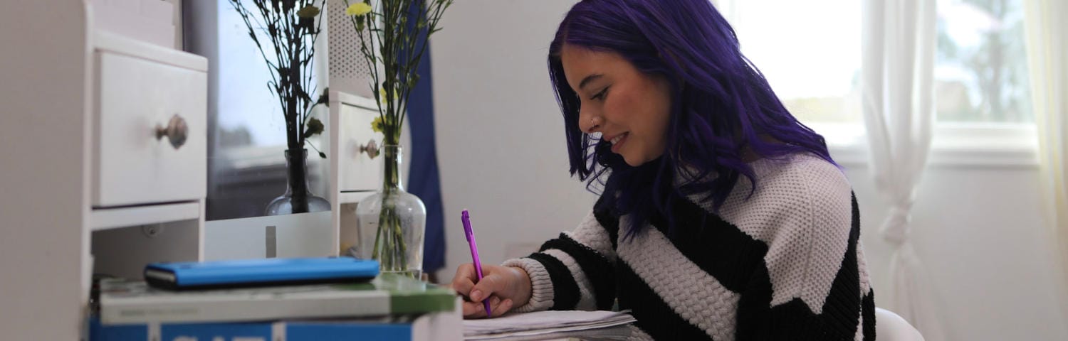 Student with purple hair taking notes at home during an online class
